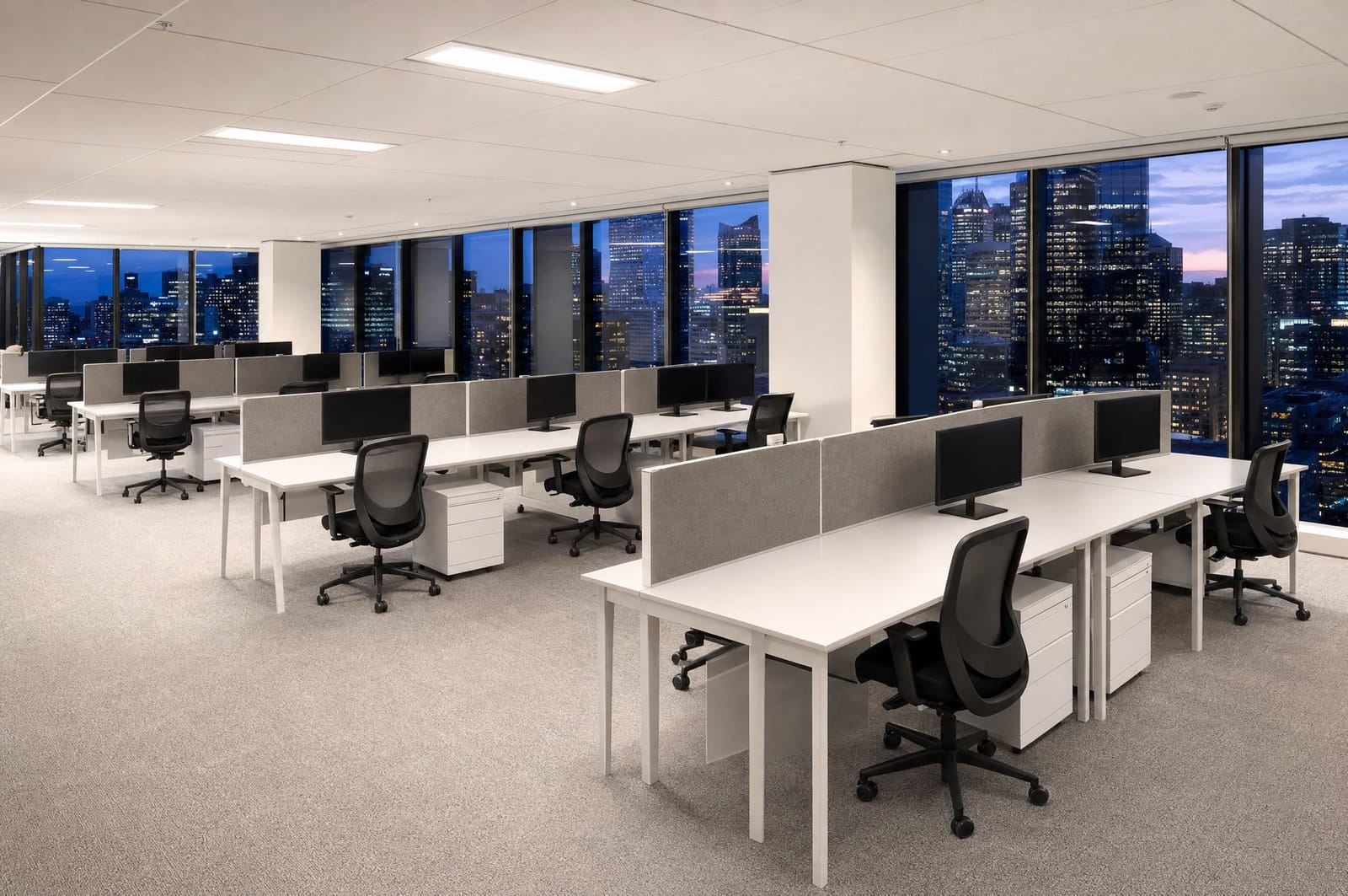 An empty open-plan office on a high floor of a Melbourne CBD tower at dusk, desks clean and the city lights coming on.