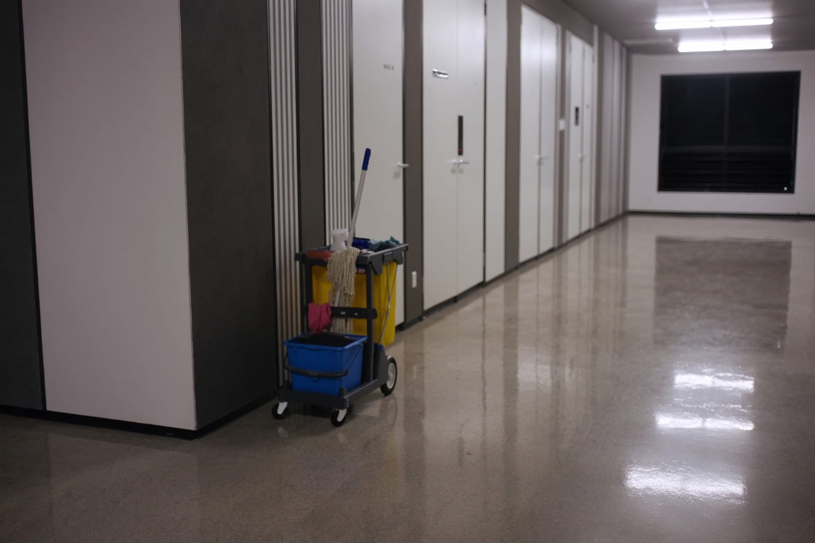 A professional cleaning trolley parked in a clean, brightly lit office corridor after hours.