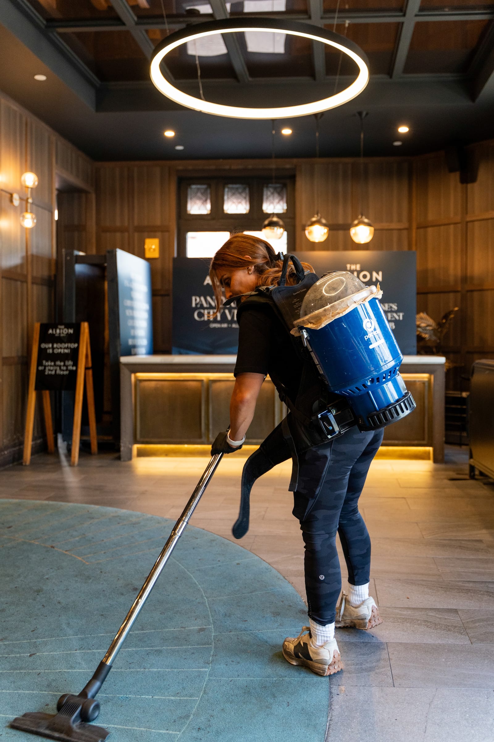 A HOZ CLEANING cleaner vacuuming a venue foyer with a backpack vacuum.