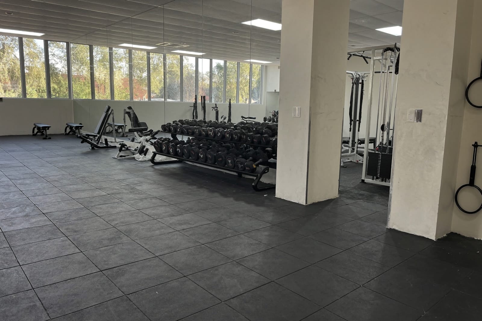 An empty boutique gym with freshly mopped rubber flooring, wiped weights and streak-free mirrors.