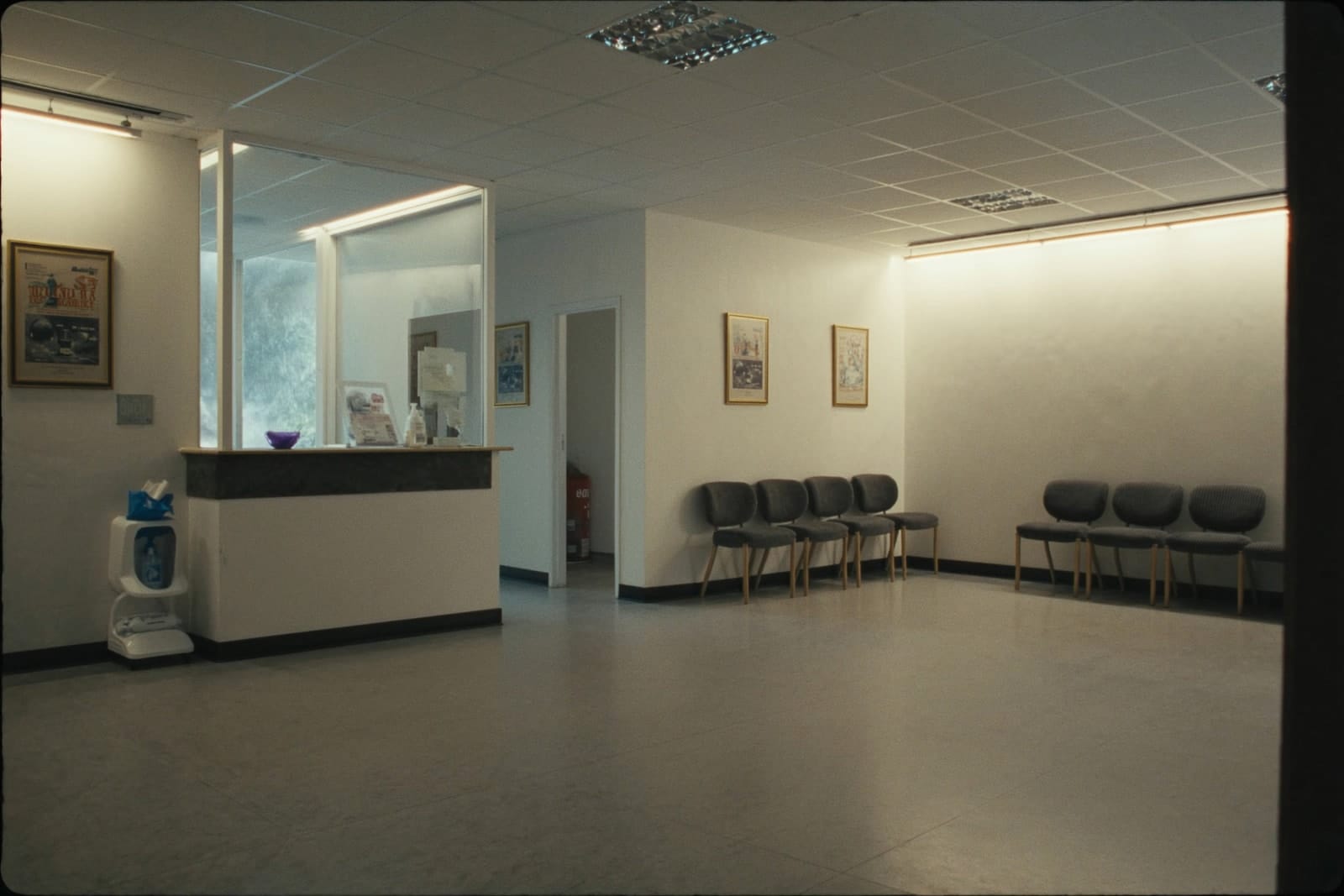 An empty, freshly cleaned medical clinic waiting room with a row of chairs and a reception desk.